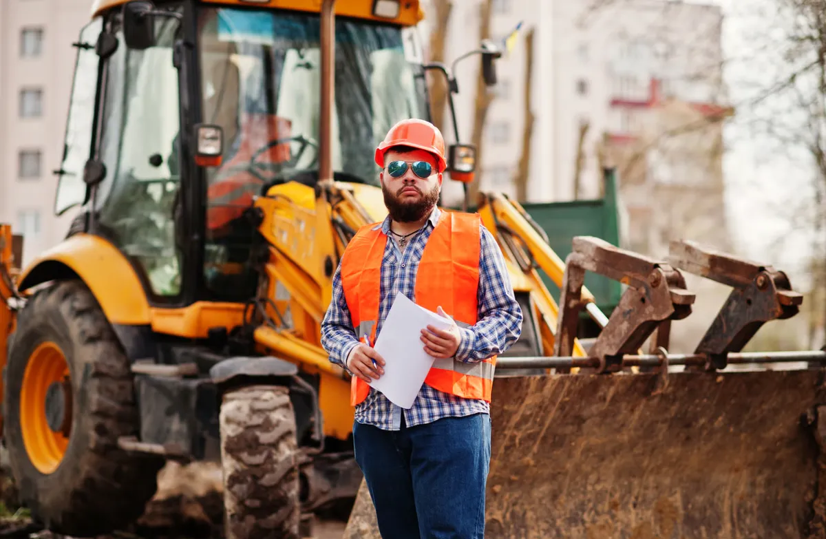 Trabajador con casco frente a una retroexcavadora