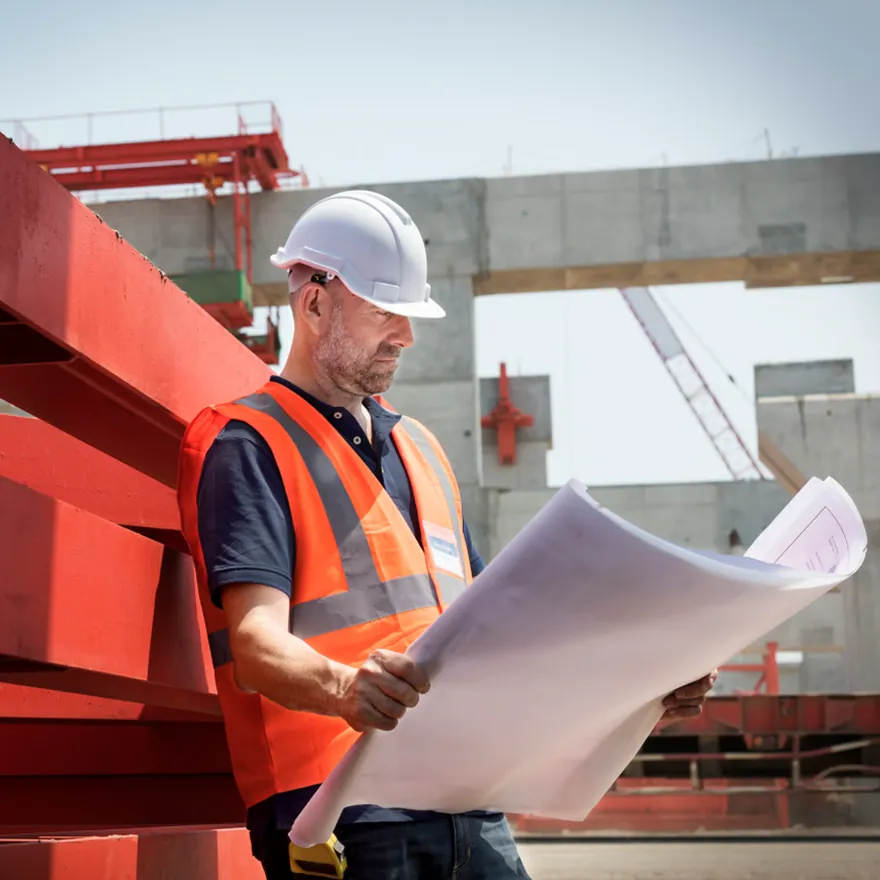Ingeniero revisando planos frente a una estructura en obra
